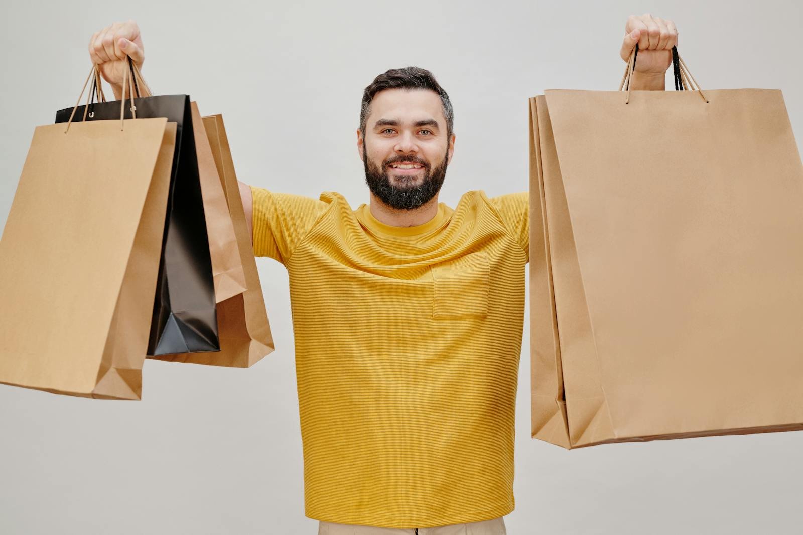 Un homme heureux en chemise jaune tenant plusieurs sacs de courses, exprimant la joie du shopping.
