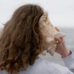 une femme aux cheveux longs tenant un coquillage devant son visage