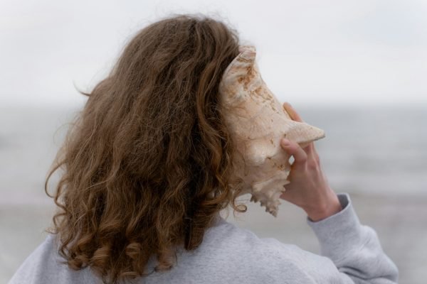 Comment choisir les meilleures aides auditives pour vos besoins ? une femme aux cheveux longs tenant un coquillage devant son visage