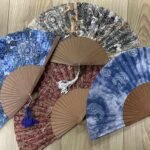 Assortiment d'éventails en tissu aux motifs traditionnels de type cachemire sur fond de bois.