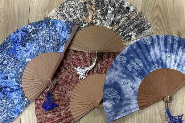 Les plus beaux motifs d’éventails en tissu : entre tradition et modernité Assortiment d'éventails en tissu aux motifs traditionnels de type cachemire sur fond de bois.