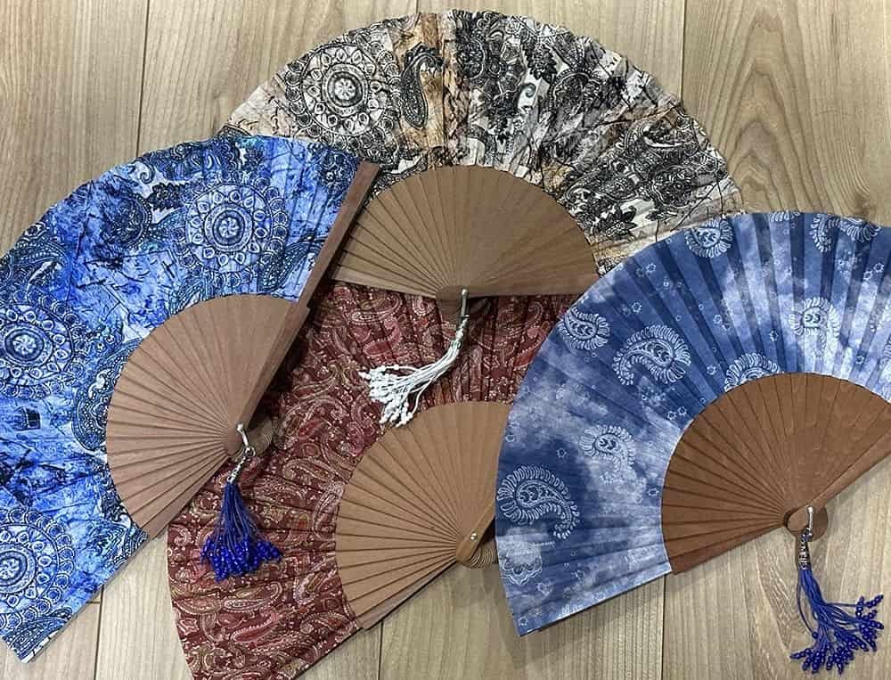 Les plus beaux motifs d’éventails en tissu : entre tradition et modernité Assortiment d'éventails en tissu aux motifs traditionnels de type cachemire sur fond de bois.