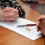 Gros plan sur les mains de deux conjoints lors d'une procédure de divorce à Chambéry, avec alliances et stylo déposés sur un dossier juridique.