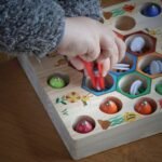 Une main utilise des pinces rouges pour placer des boules colorées
