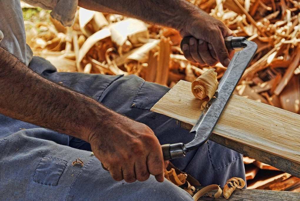 Homme sciant une planche de bois au-dessus de copeaux de bois