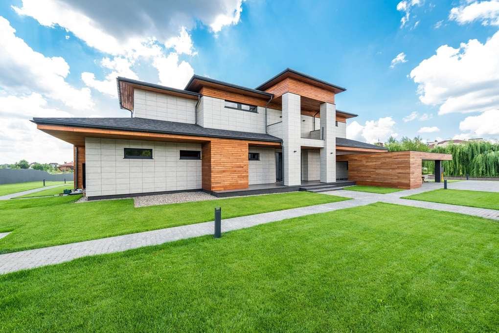 Maison contemporaine avec façade en bois et brique, toiture plate, entourée d'une pelouse bien entretenue sous un ciel ensoleillé
