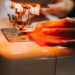 Main guidant un tissu rouge sous une aiguille de machine à coudre blanche