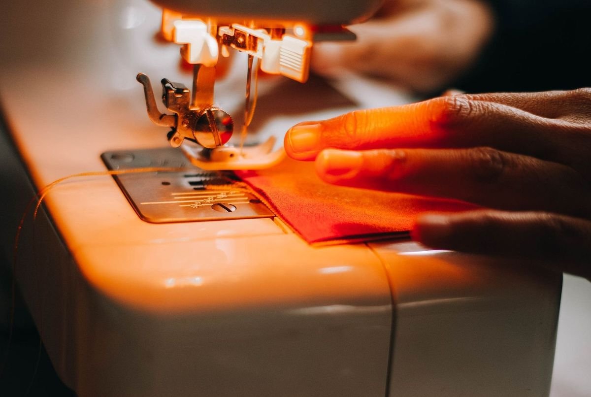 Main guidant un tissu rouge sous une aiguille de machine à coudre blanche