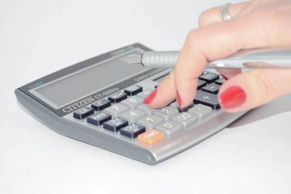 Une main aux ongles rouges appuie sur une calculatrice avec un stylo