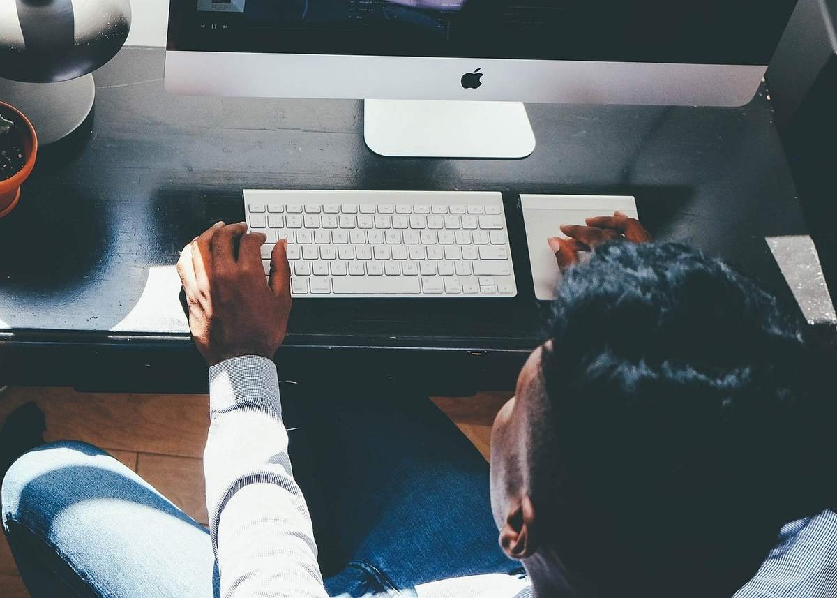 Personne assise devant un ordinateur iMac, utilisant clavier et souris
